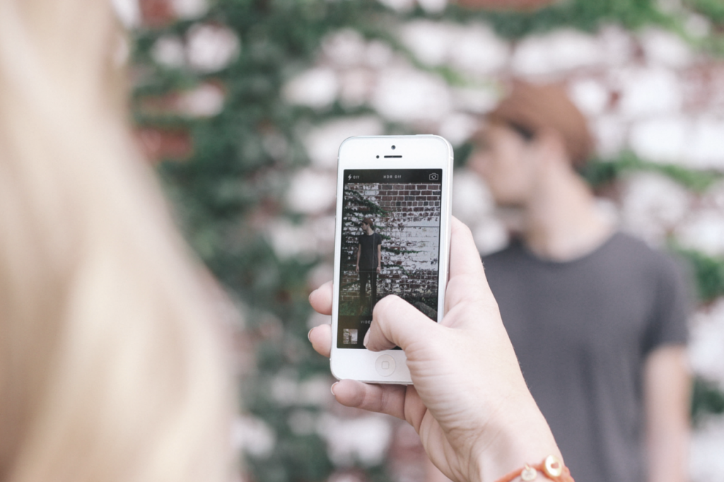 Young woman taking photo of a young man with an iPhone