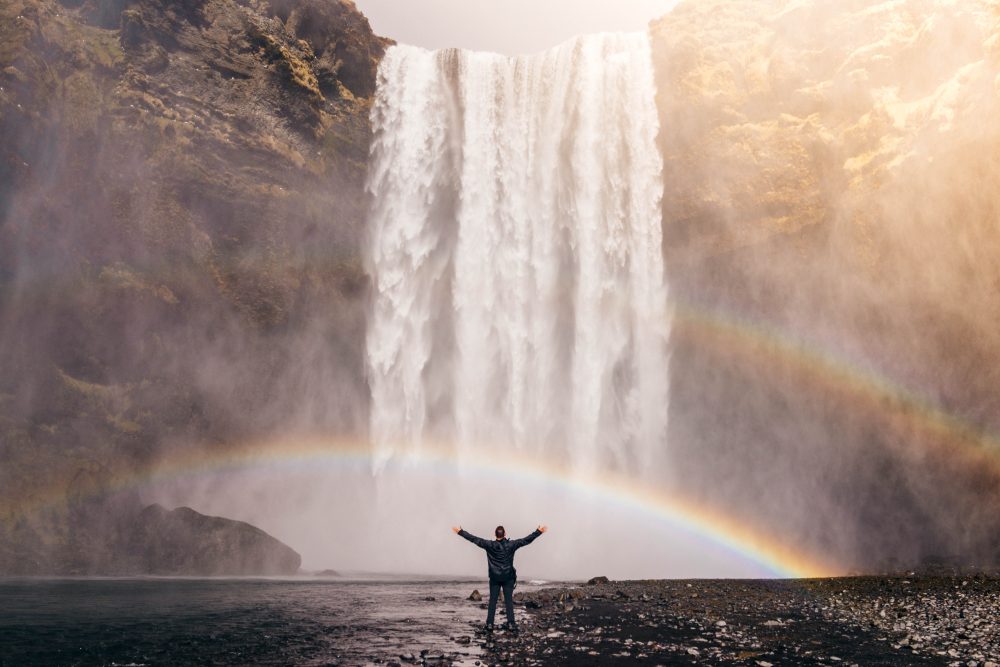 Person standing under a waterfall with a rainbow